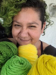 woman smiling holding green and yellow skeins of yarn